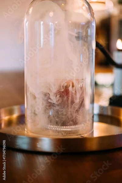 Fototapeta Preparing alcoholic beverage. Pub glassware. Cocktail covered with transparent dome on bar counter. Smoking gun device for flavor.