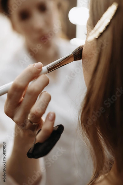 Fototapeta Makeup artist applying blush or highlighter to model face. Close-up vertical