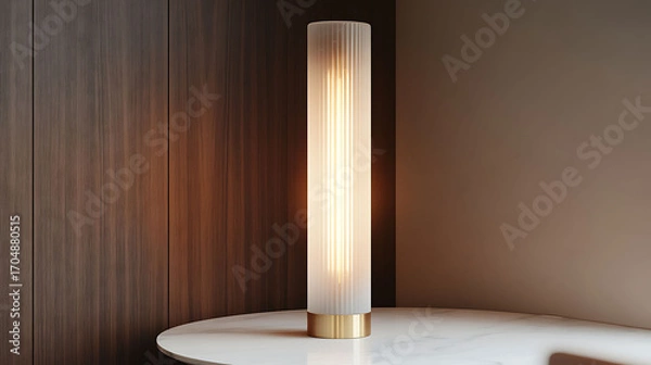 Fototapeta Tall, slender lamp with a frosted vertical tube design and brass base, softly illuminating a white marble tabletop in a modern corner
