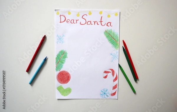 Fototapeta Children's drawing of Dear Santa letter with drawings of fir branches, Christmas ornaments, snowflakes, candy cane on white surface. On white table, surrounded by colored pencils. Top view. Template.