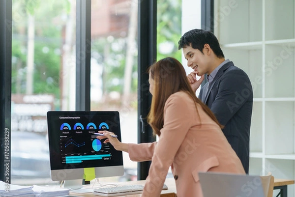 Fototapeta Businesswoman pointing at computer screen showing charts and graphs while discussing with businessman in modern office