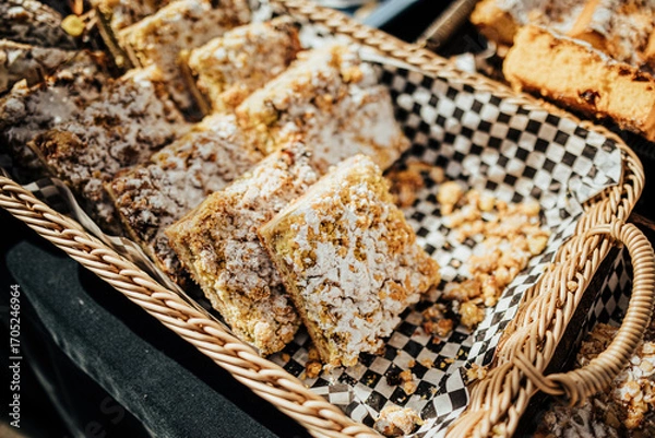 Fototapeta An assortment of pastries, muffins, and baked goods displayed in baskets and trays at an outdoor market stall, sprinkled with sugar and nuts for a rustic treat