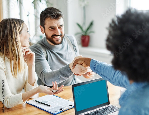 Fototapeta Portrait of a young couple shaking hands and closing a deal for aa new property purchase with real estate agent in her office