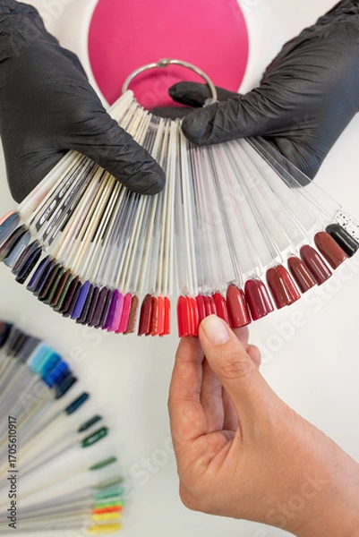 Fototapeta A hand holds a fan of nail polish colors, showcasing a diverse range of shades for manicure selection in a salon