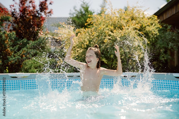 Fototapeta A cheerful boy splashes in the pool under a bright blue sky. He interacts playfully with water, enjoying quality time with his dad and brother in a lively backyard setting.