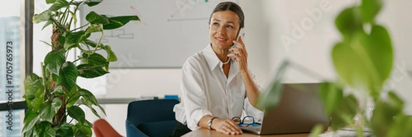 Fototapeta A professional businesswoman is working in a modern office environment while making a phone call