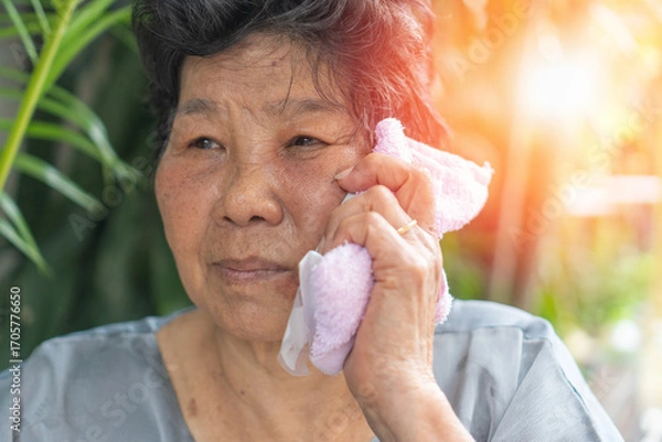 Fototapeta Elderly woman using a towel with ice pack on her face for pain relief, showing home healthcare, self-care, and senior lifestyle in managing discomfort, swelling, headache, tooth problem, dental care
