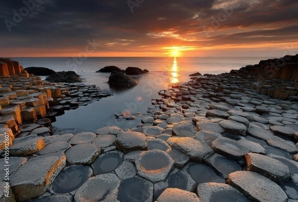 Fototapeta Hexagonal basalt columns meet the ocean under a dramatic sunset sky. Warm colors and textures create a captivating scene