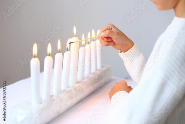 Fototapeta the ritual of lighting candles on the menorah during Hanukkah. The flames flicker gently, casting a warm glow that symbolizes hope and miracles. This cherished tradition brings families together