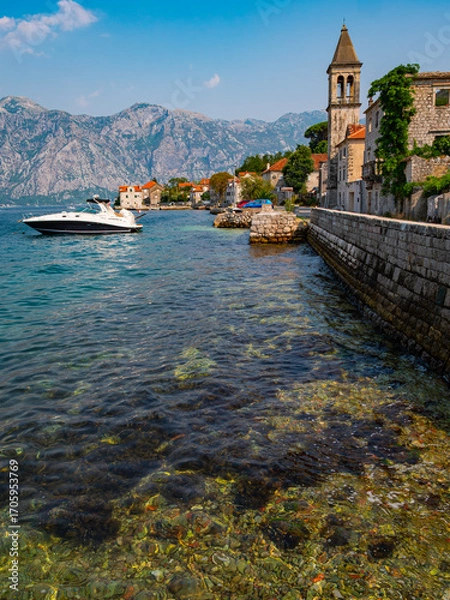 Fototapeta The Catholic church of Saint Basil and a row of stone buildings at Donji Stoliv on the Bay of Kotor shoreline in Montenegro. Mountains rise in background. 
