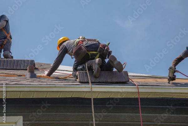 Obraz Construction Workers with Safety Equipment Installing Asphalt Shingles on Residential Roof