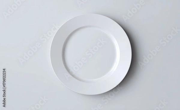 Fototapeta A clean, white, round plate sits centered, slightly askew on a plain, bright, white surface in soft, even lighting