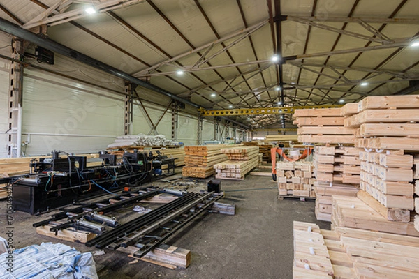 Fototapeta Large warehouse with stacks of wood, machinery, and a high ceiling structure