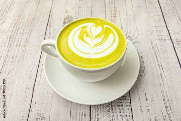 Fototapeta A clear cup with a modern, frothy matcha latte, viewed from above against a light brown background, highlighting its texture and green hue