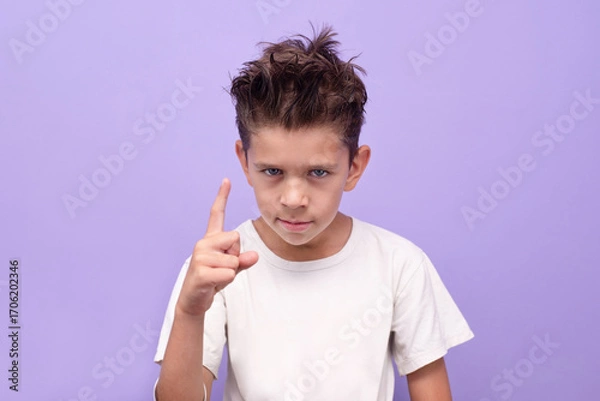 Fototapeta Boy pointing warning gesture on lilac background expressing emotion and communication. A young boy emphasizes something or strictly indicates that this is not allowed