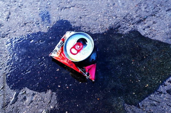 Fototapeta Spilled drink from Crumpled Beer Can. Discarded broken carbonated drink tin can on asphalt road. Thrown out Crushed juce. Crumpled soda can on asphalt with drink spilled. Crushed bottle.