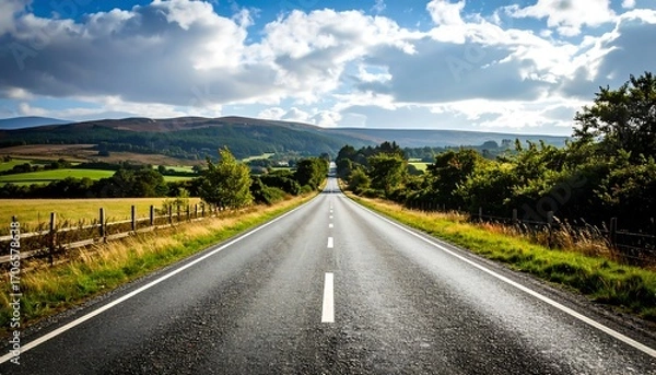 Fototapeta Empty road stretching into a landscape of hills and trees under a partly cloudy sky