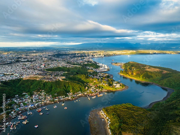 Obraz An aerial view of Puerto Montt Canal de Tenglo during the afternoon, with a mix of golden light and dramatic shadows on the landscape under a cloudy sky.