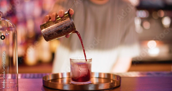 Fototapeta Serving drink. Preparing liquor. Bartender pouring red strained liquid from metal shaker. Professional making refreshing beverage.