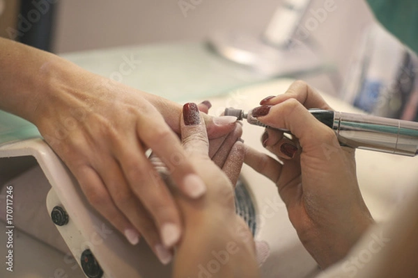 Fototapeta The process of manicure at a beauty salon with electrical  file.  Close up.