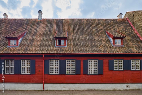 Fototapeta Traditional red wooden house with black shutters and tiled roof, featuring small dormer windows. Historic European architecture.