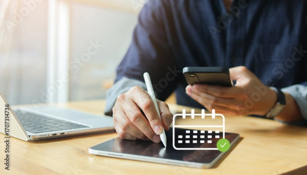 Fototapeta Close up hand using stylus on tablet with calendar icon, while holding smartphone. Digital scheduling, on online appointment or business planning for time management and productivity concept