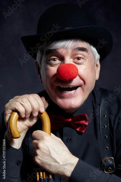 Fototapeta Portrait of laughing  clown against a dark background leaning on the handle of an umbrella.