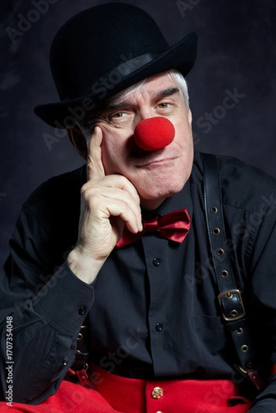 Fototapeta Dramatic portrait of a sad clown against a dark background. Hand near face.