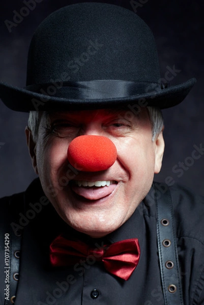 Fototapeta Portrait of a clown with a hat pulled down over his eyes sticks out his tongue.
