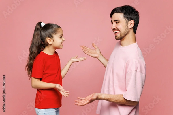 Fototapeta Side view young smiling parent man with child girl wearing red casual clothes. Daddy little kid daughter talk speak with each other isolated on plain pink background. Father's Day Love family concept.