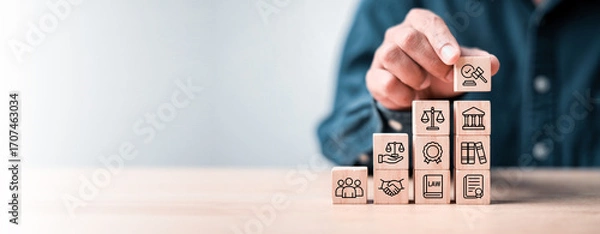 Fototapeta Business hand stacking wooden blocks with law and justice icons on light background. Concept of legal service, justice system, compliance, and business law consulting.