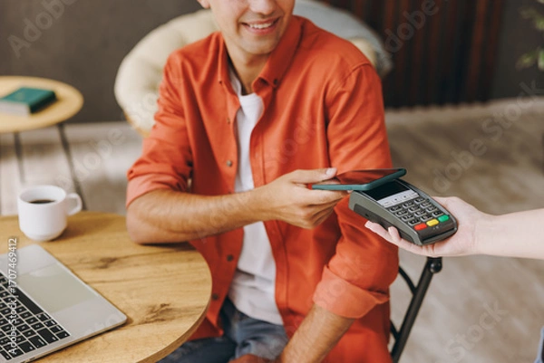 Fototapeta Young happy man wear casual clothes hold bank payment terminal process acquire cell phone sit at table in coffee shop cafe relax rest in restaurant in free time indoor Freelance mobile office concept.