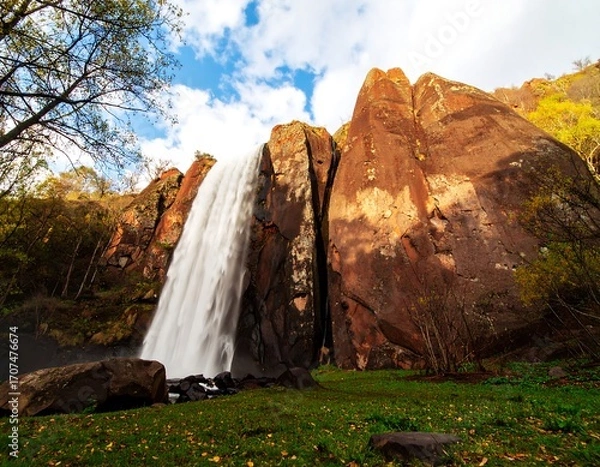 Fototapeta Waterfall cascading down red rock cliffs in autumn foliage