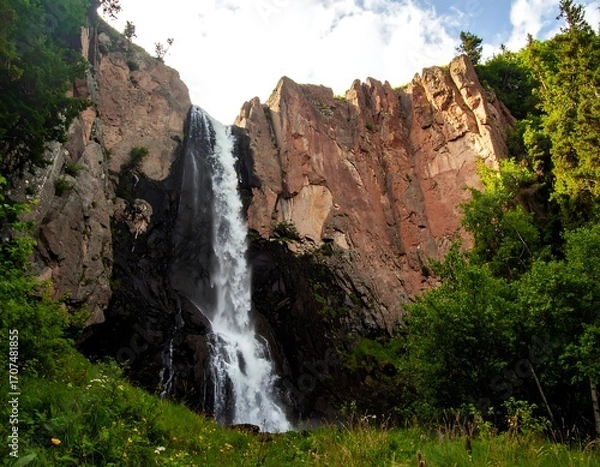 Fototapeta Waterfall cascading down rocky cliff face, lush forest backdrop