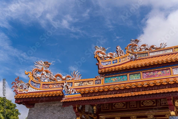 Fototapeta A close-up shot captures the exquisite craftsmanship of an ancient Hue palace, with vibrant, ornate dragon statues and a mosaic of colors against a brilliant blue sky.