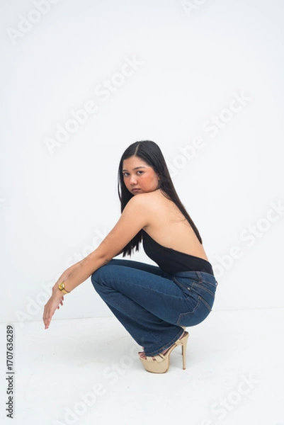 Fototapeta An expressive young Asian woman captured from the side, crouching with a fierce editorial pose and striking, powerful eyes. Isolated on a white background.