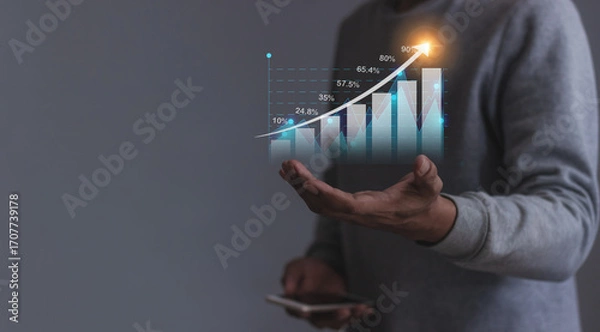 Fototapeta Young man with smartphone hand holding to visualize money growth The phone screen displays graphs and charts showing increasing investment and savings trends, along with an increased account balance