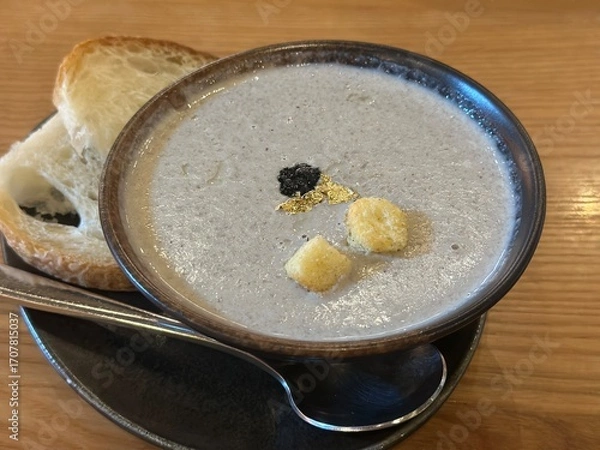 Obraz A rich and creamy Truffle Mushroom Soup served in a rustic bowl, garnished with black truffle bits and croutons, accompanied by toasted bread slices on a wooden table.