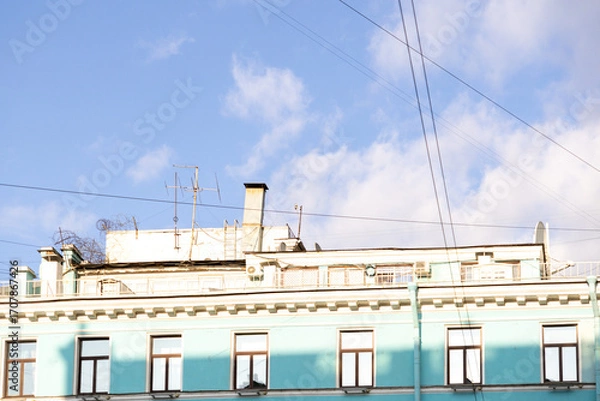 Fototapeta Urban life, a house with blue walls after restoration. A blue sky with a few clouds and a building with a chimney. The sky is clear and bright, the building is painted blue.