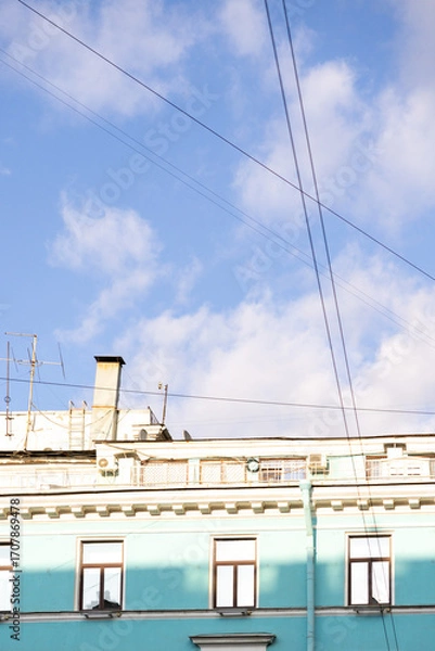 Fototapeta Urban life, a house with blue walls after restoration. A blue sky with a few clouds and a building with a chimney. The sky is clear and bright, the building is painted blue.