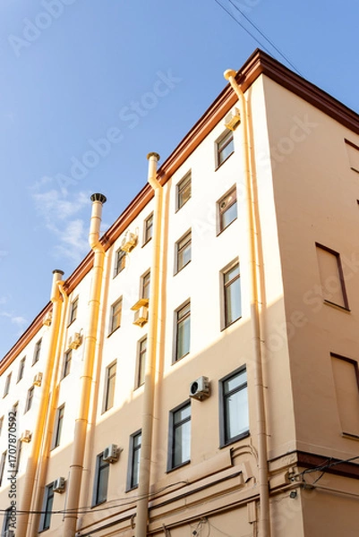 Fototapeta Air conditioners on the facade of a yellow house against a blue sky. An air ventilation and cooling system and air purification technologies are installed. split system.