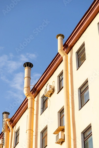 Fototapeta Air conditioners on the facade of a yellow house against a blue sky. An air ventilation and cooling system and air purification technologies are installed. split system.