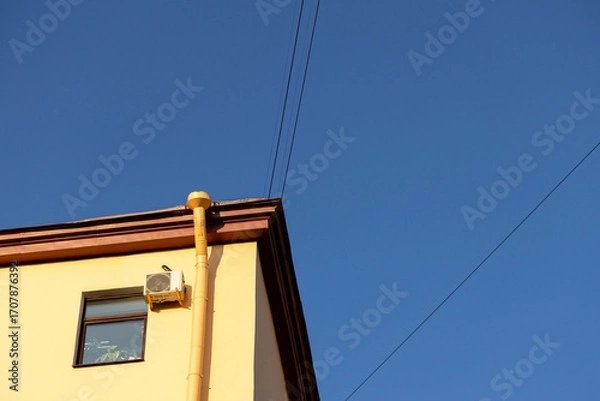 Fototapeta Air conditioners on the facade of a yellow house against a blue sky. An air ventilation and cooling system and air purification technologies are installed. split system.