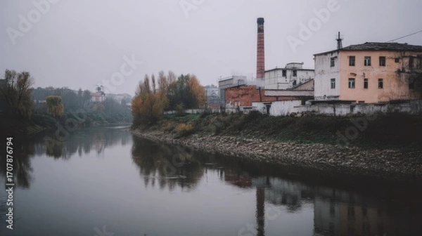 Fototapeta Tranquil River Scene with Industrial Building Reflection on Water in Overcast Weather with Autumn Foliage and Calm Atmosphere