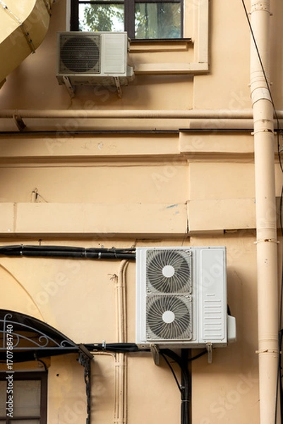Fototapeta Air conditioners on the facade of yellow historical house. An air ventilation and cooling system and air purification technologies are installed. split system. cooling in hot weather. climate.