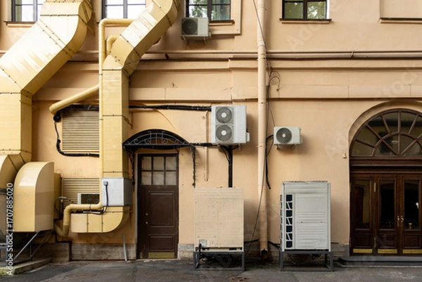 Fototapeta Air conditioners on the facade of yellow historical house. An air ventilation and cooling system and air purification technologies are installed. split system. cooling in hot weather. climate.