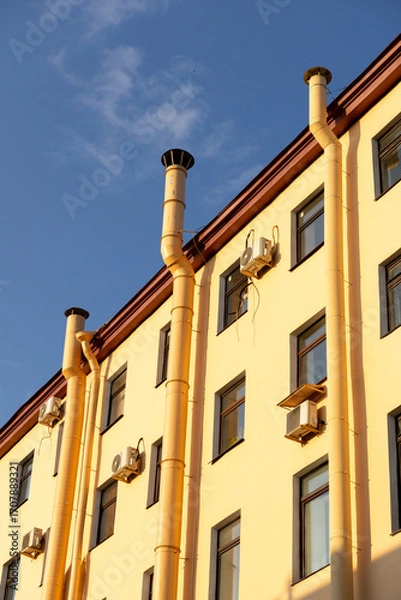 Fototapeta Air conditioners on the facade of a yellow house against a blue sky. An air ventilation and cooling system and air purification technologies are installed. split system.