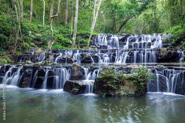 Fototapeta Samlan Waterfall, tier 1, tropical waterfall cascading over layered black rocks in lush rainforest of Thailand.