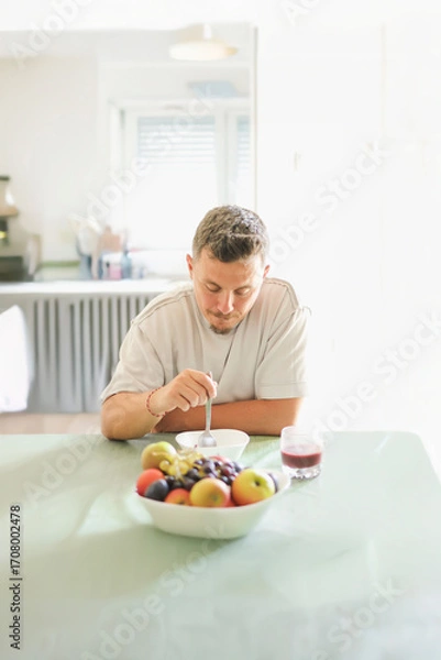 Fototapeta Man Enjoying Organic Cereal in a Bright Kitchen.