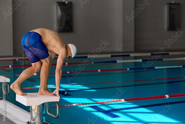 Fototapeta Swimmer bending on starting block before diving into pool for competitive race. Concept of professional sports, preparation, focus, editorial visuals, motivation, and competitive energy.